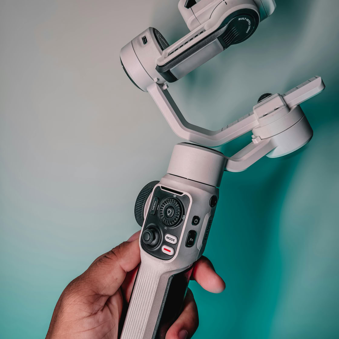 A person holding a gimbal stabilizer for mobile photography in a studio setting.