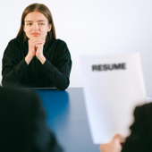 A woman in a job interview facing two employers with a focus on her resume.